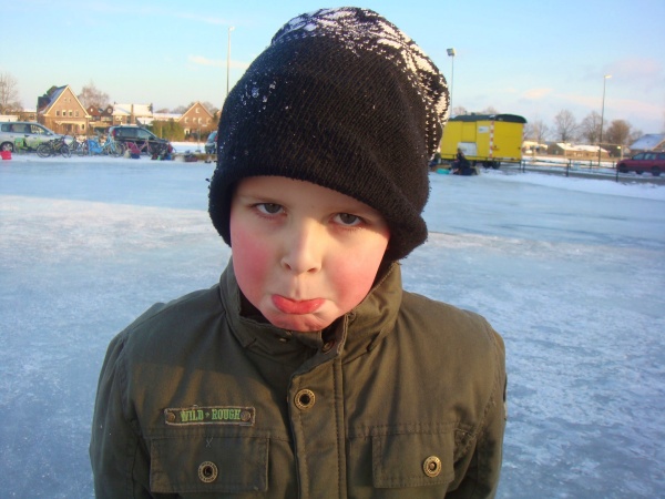 Seasonal Changes. Young boy outside in winter with coat, hat, red cheeks and frowning.